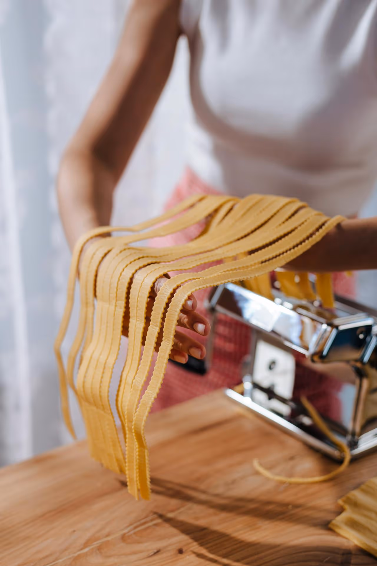Woman making fresh pasta with a machine. 
