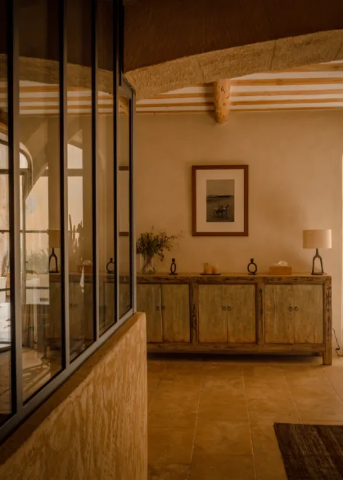 Rustic interior with wooden sideboard, lamp, photo frame, and large black framed windows.