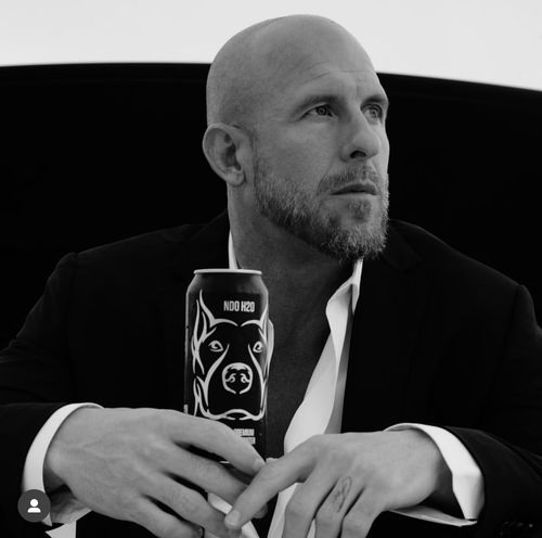 Bald man with a beard wearing a suit holds a can with a dog illustration while looking to the side.