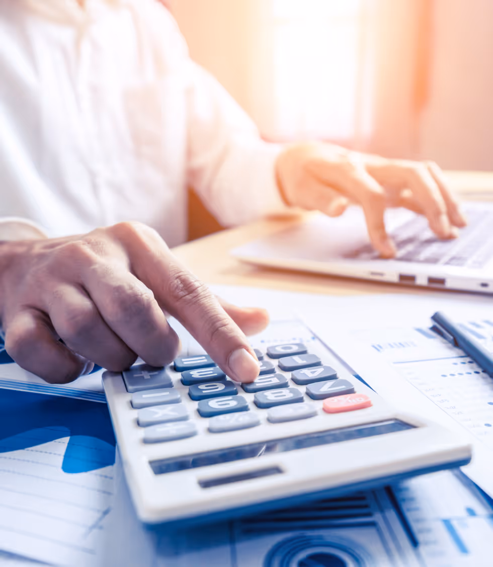 She Knows Alt Text said:
Close-up of a person using a calculator with one hand while typing on a laptop with the other. Blue-toned financial charts and graphs are spread across the desk, indicating financial analysis or budget planning.