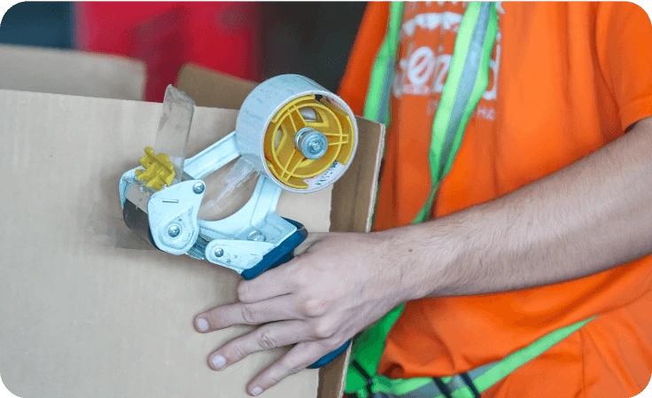 Worker sealing cardboard box with packing tape at Palletized warehouse