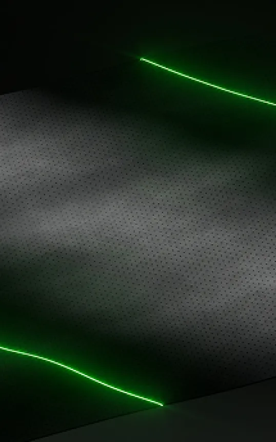 Close-up of a black perforated surface with bright green neon light strips along the edges.