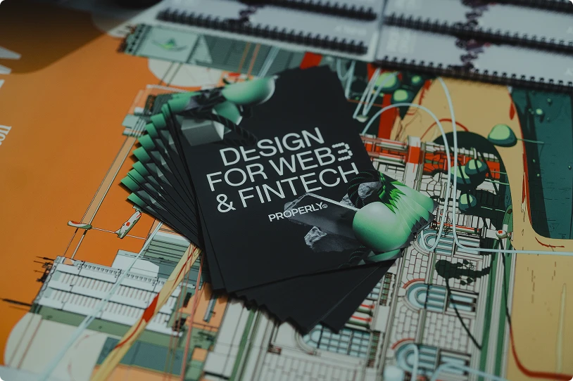Stack of black brochures with text 'DESIGN FOR WEB3 & FINTECH PROPERLY' on a colorful abstract map background.