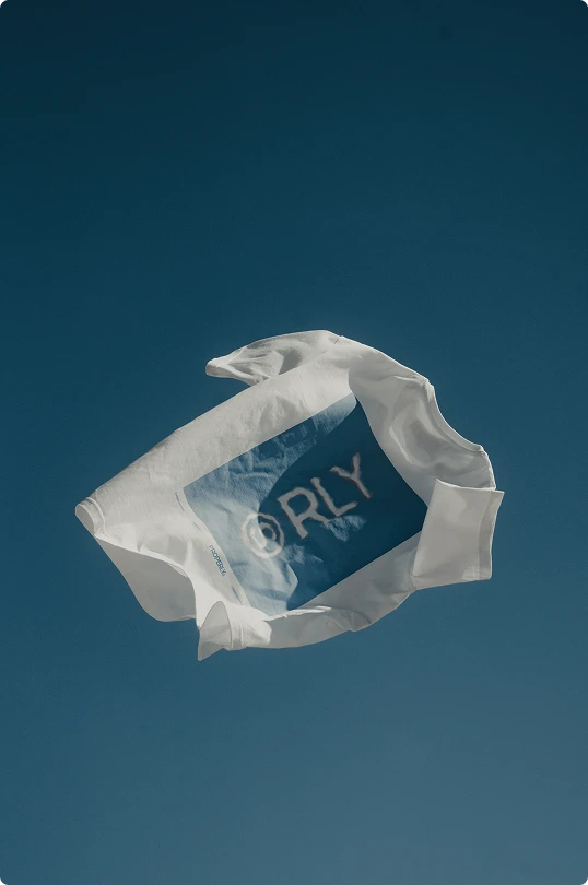 White t-shirt with a blue square and partially visible text floating against a clear blue sky.