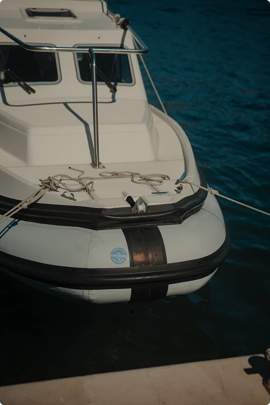 Close-up of the front of a white inflatable boat tied to a dock on calm blue water.