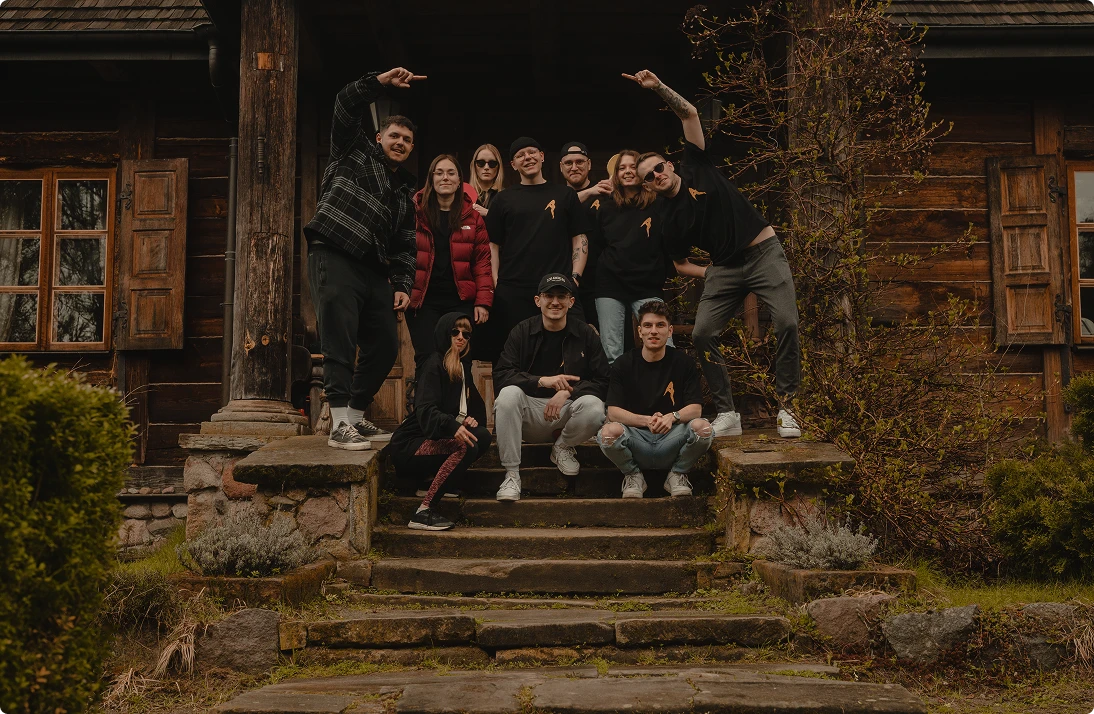 Group of ten young adults posing on stone steps in front of a rustic wooden house.