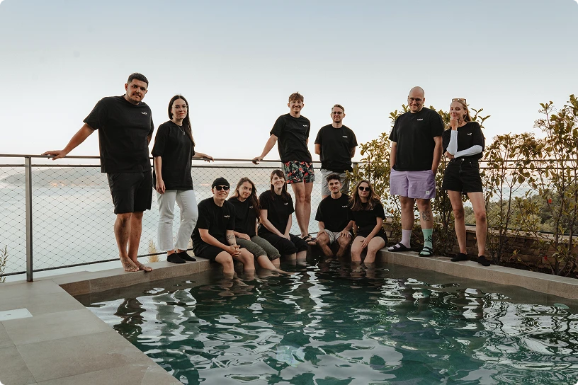 Group of ten casually dressed people posing around a pool with a scenic water view in the background.