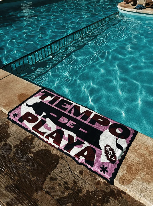 A colorful towel with the text 'TIEMPO DE PLAYA' laid out beside a clear blue swimming pool.