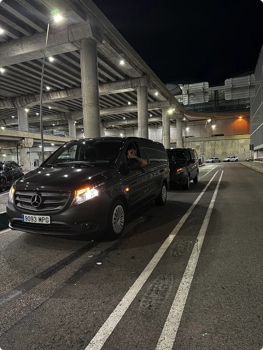 Black Mercedes van with headlights on parked under an overpass at night.