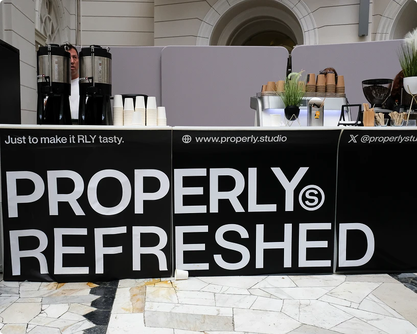 Coffee stand with black banners reading 'PROPERLY REFRESHED' and coffee cups and dispensers on the counter.