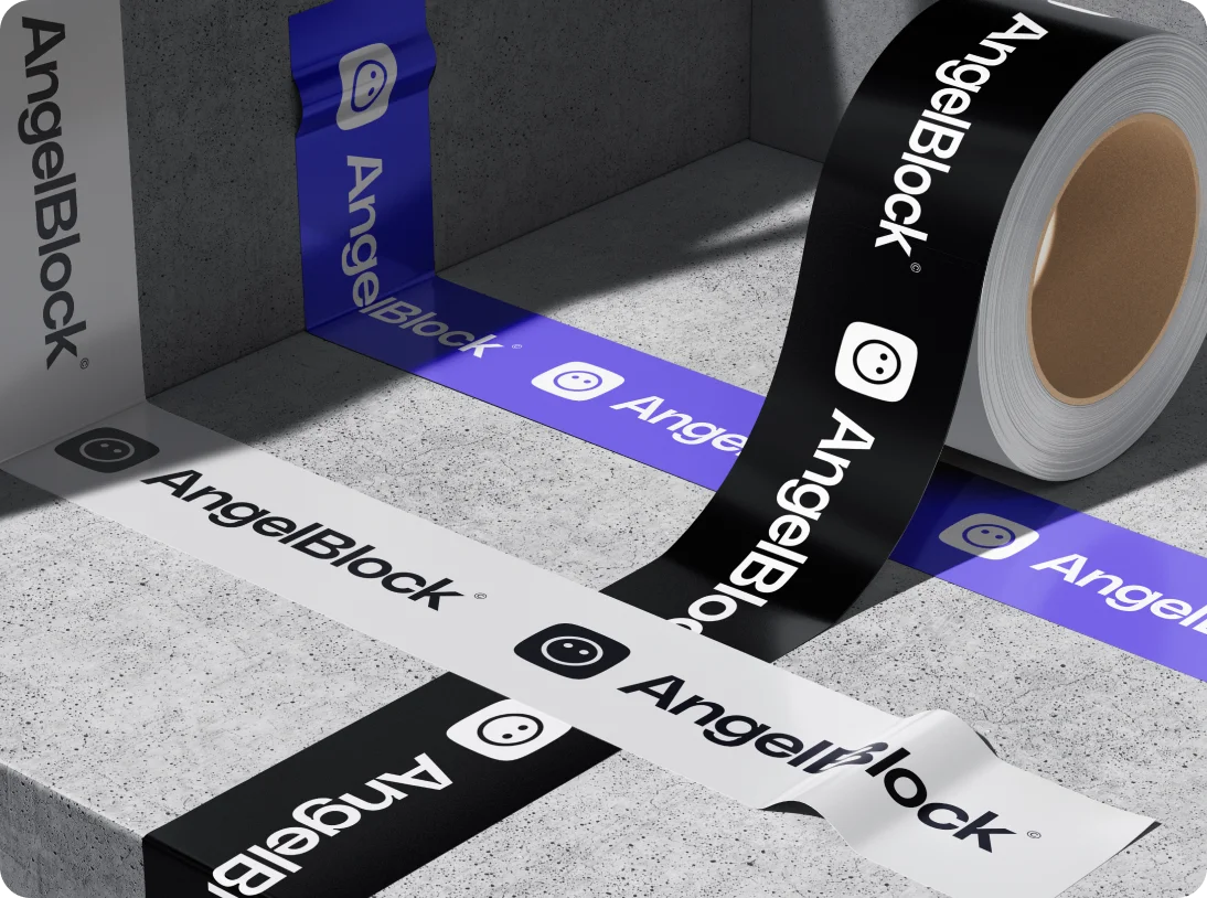 Rolls of adhesive tape in black, white, and blue with AngelBlock logo and text on a concrete surface and wall.