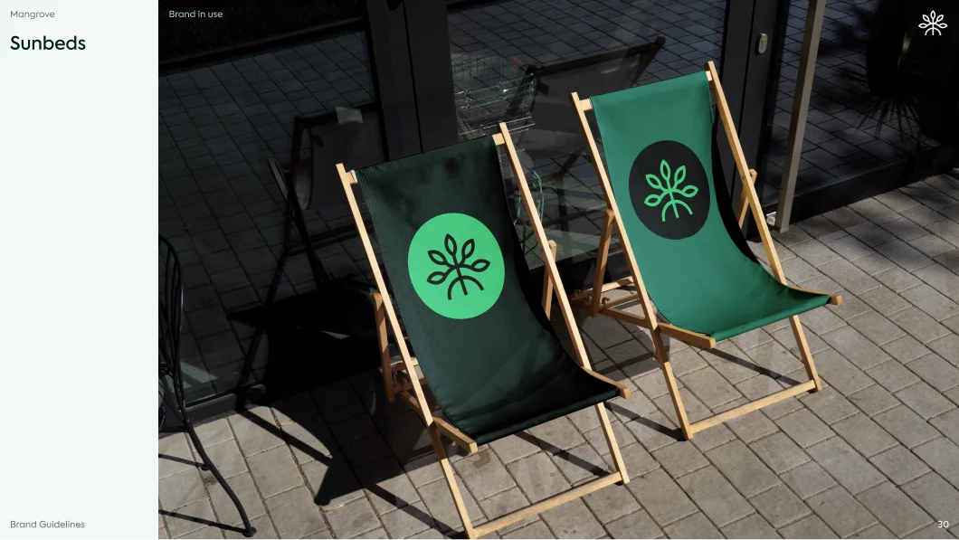 Two wooden sunbeds with green fabric displaying a leaf logo, placed on a tiled patio outside glass doors.