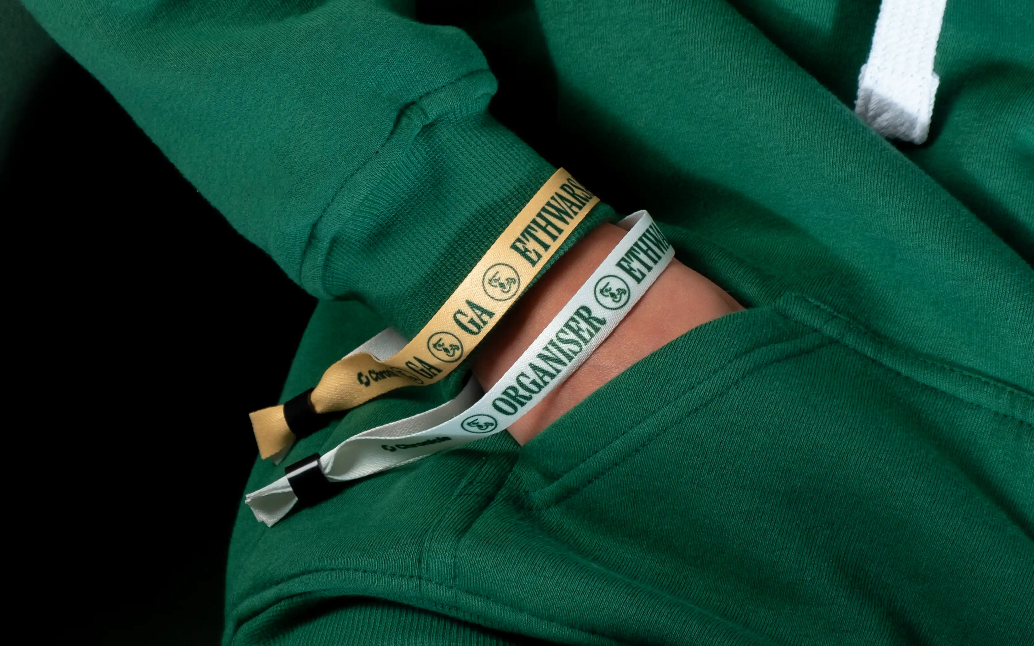 Person wearing a green hoodie with two fabric wristbands, one beige and one white, both labeled 'ETHWARDS'.