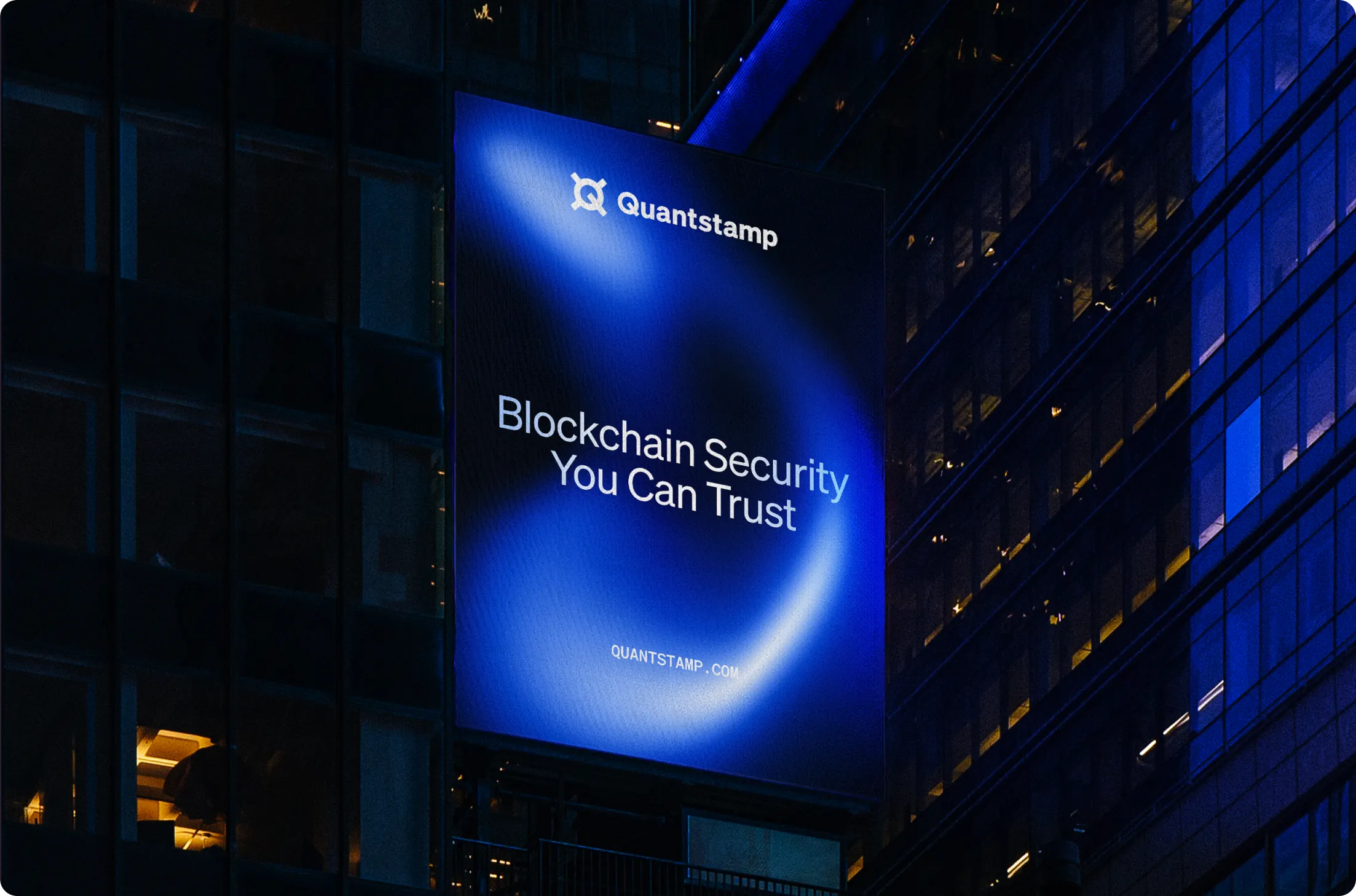 Large illuminated billboard on a building at night displaying Quantstamp logo and the text 'Blockchain Security You Can Trust'.
