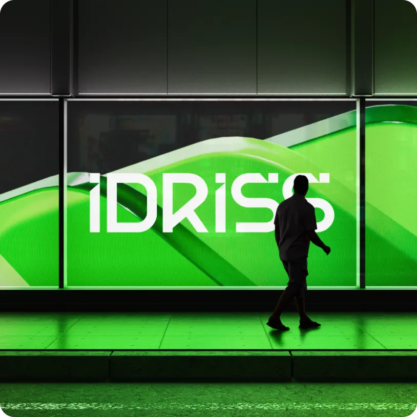 Silhouette of a person walking in front of a large illuminated green sign displaying the word 'IDRISS'.