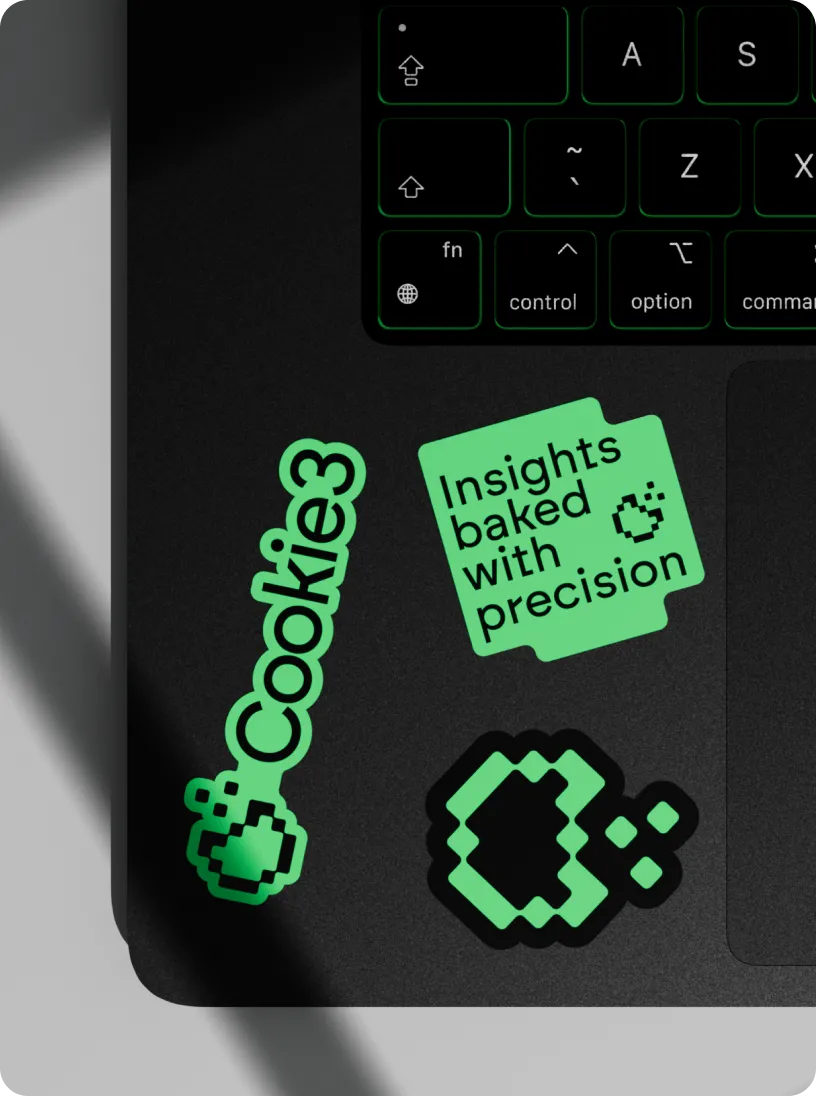 Green stickers on a black laptop near keyboard, including pixelated heart designs and text saying 'Cookie3' and 'Insights baked with precision'.