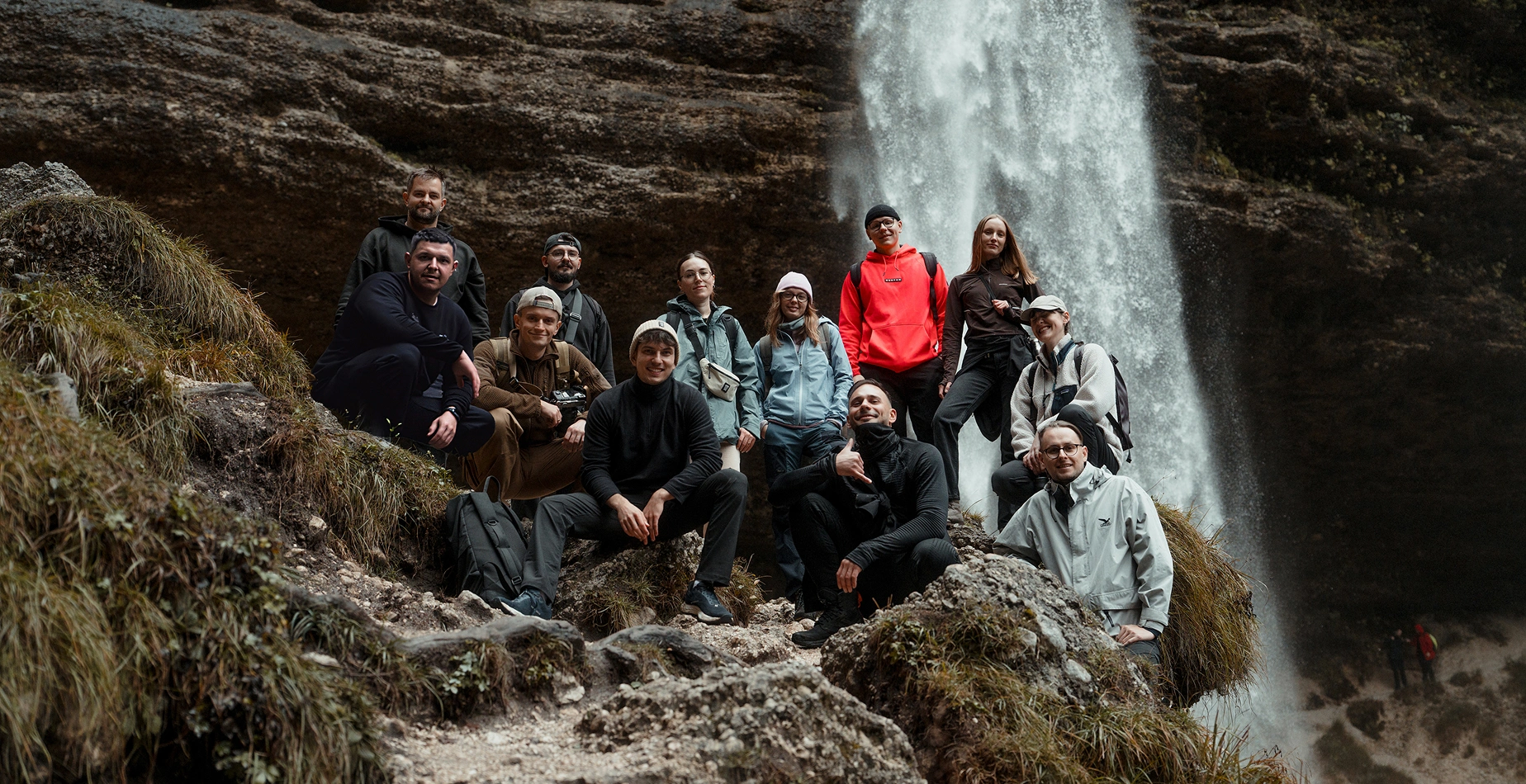 Group of twelve hikers posing on rocky terrain in front of a large waterfall.