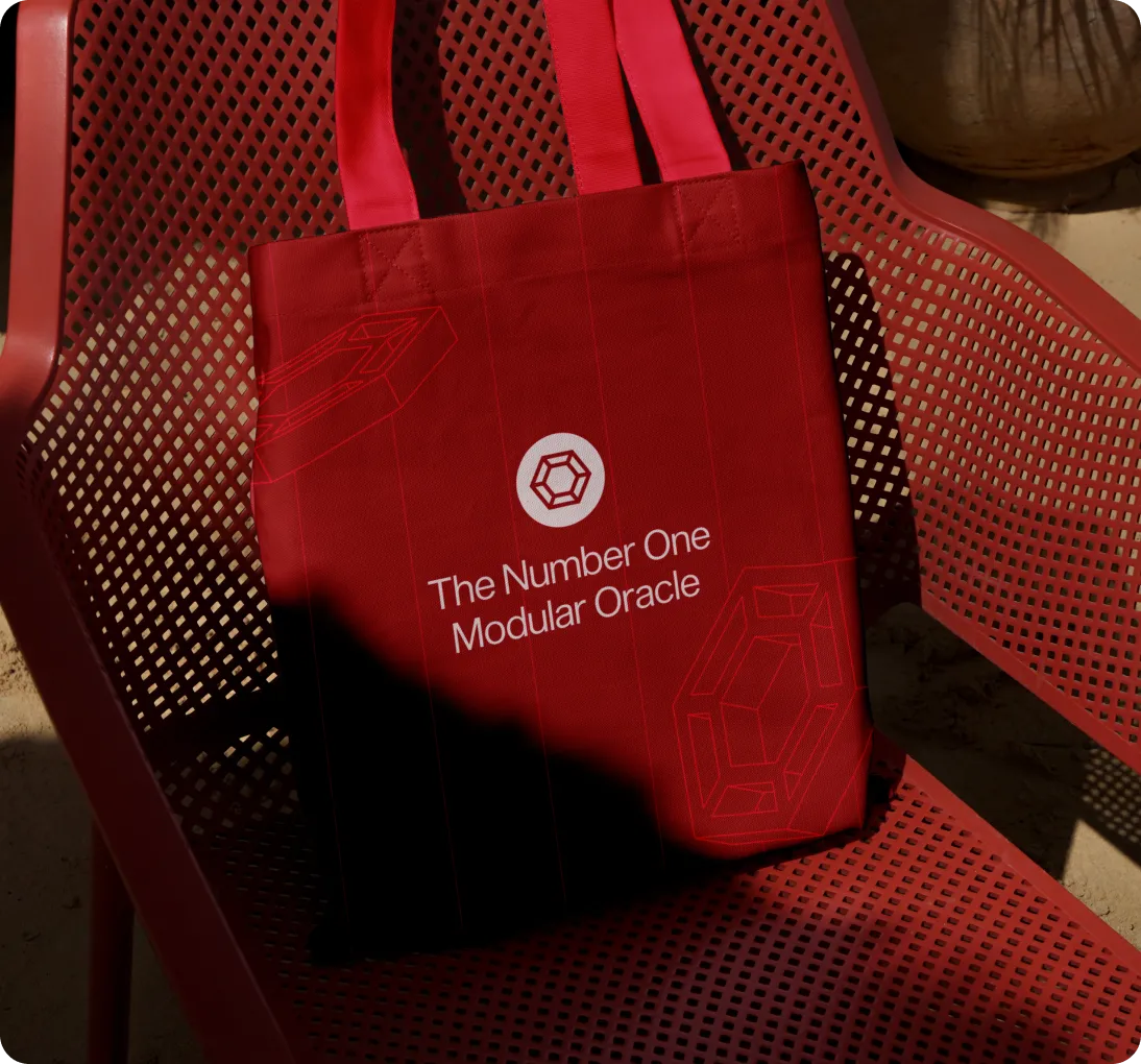 Red tote bag with the text 'The Number One Modular Oracle' and geometric designs, placed on a red metal mesh chair.