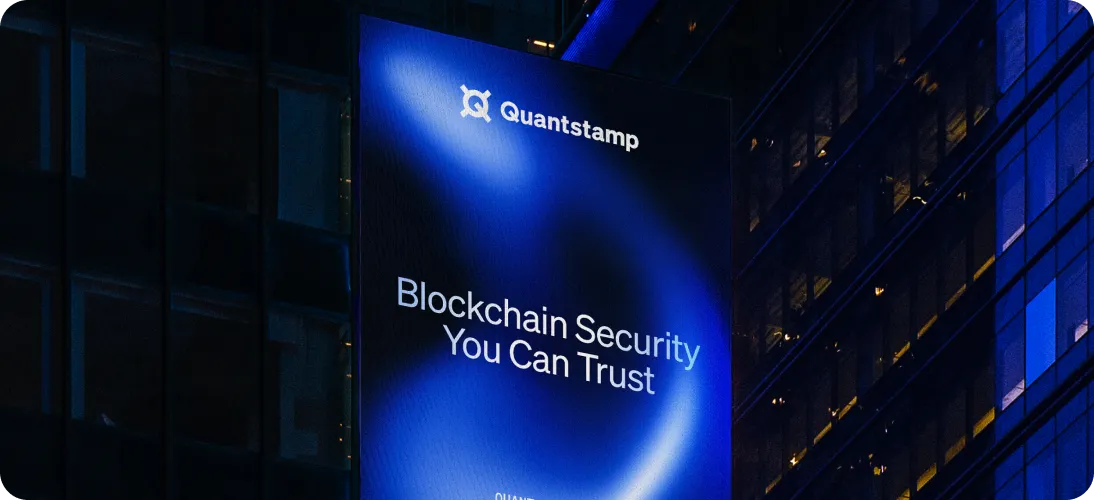 Illuminated blue billboard at night displaying the text 'Quantstamp Blockchain Security You Can Trust' on a building facade.
