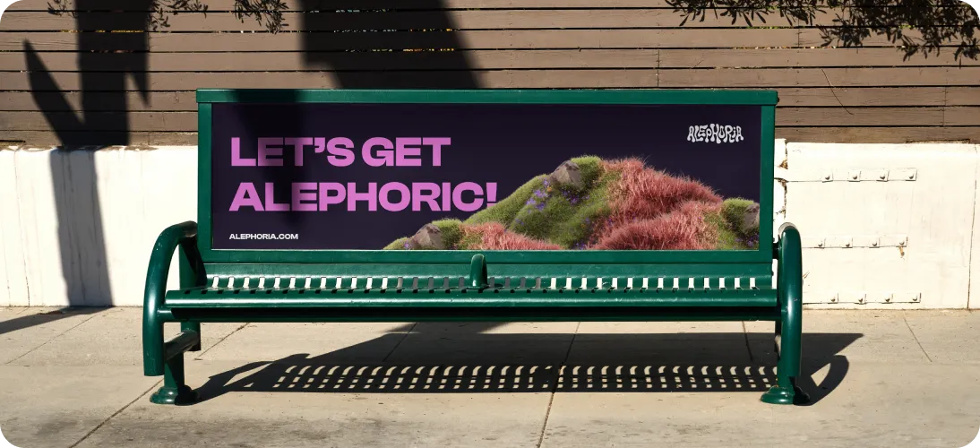 Green bench with an advertisement reading 'LET'S GET ALEPHORIC!' alongside a moss-covered sculpture of a reclining human figure.