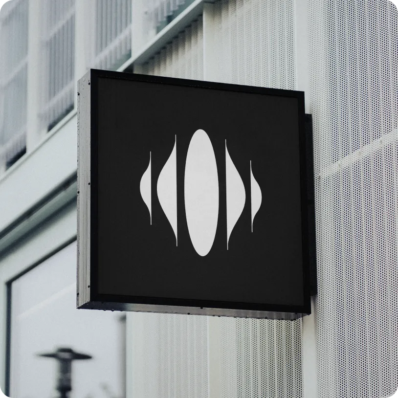Black square sign with a white abstract symmetrical design, mounted on a perforated metal wall outdoors.