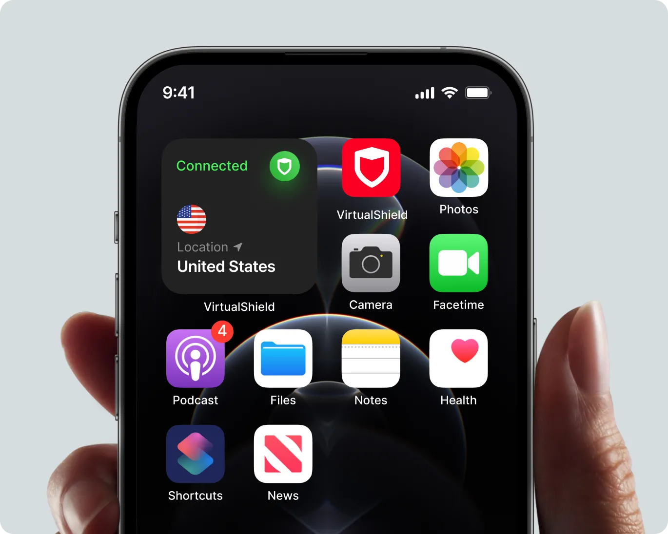 Close-up of a smartphone screen displaying a VirtualShield VPN app connected to a US server, with other app icons like Photos, Camera, Facetime, Podcast, Files, Notes, Health, Shortcuts, and News.