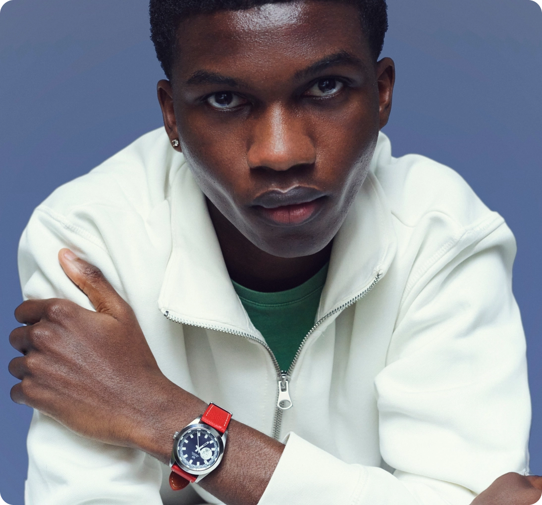 Young man wearing a white zip-up jacket and a red-strapped wristwatch, looking directly at the camera.