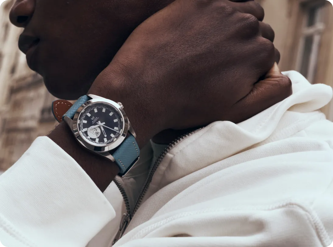 Close-up of a person wearing a silver wristwatch with a blue leather strap and black dial, adjusting their collar of a white jacket.