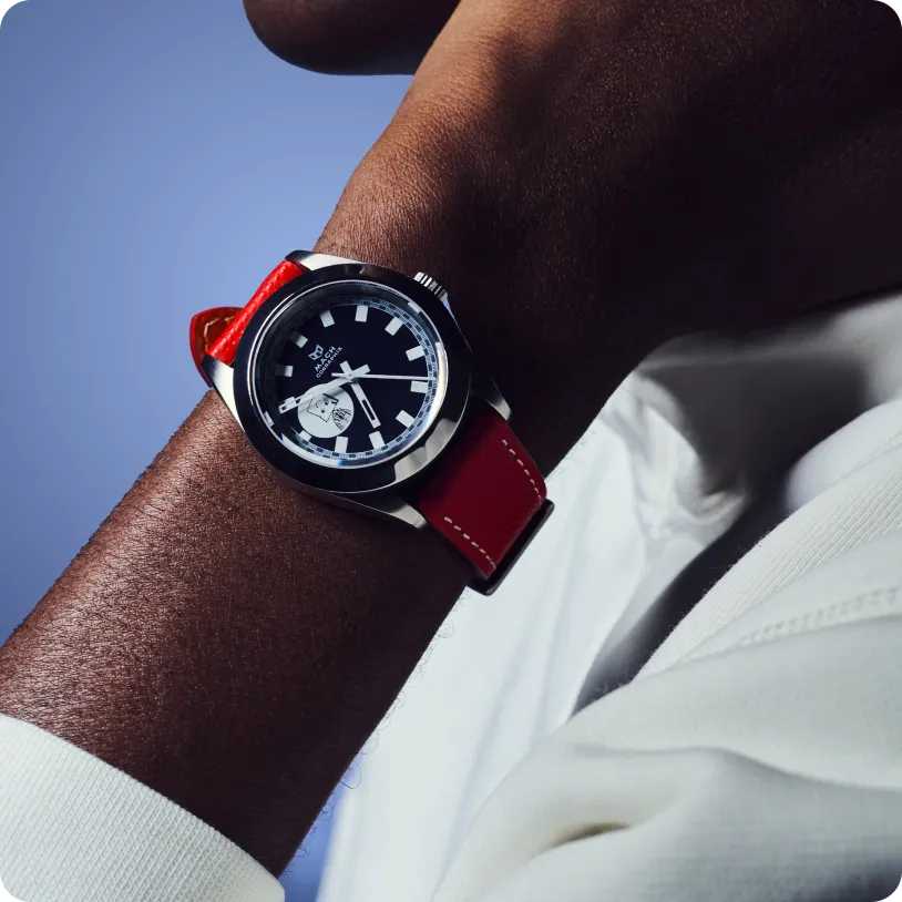 Close-up of a wristwatch with a black dial and red leather strap worn on a person's dark-skinned wrist.