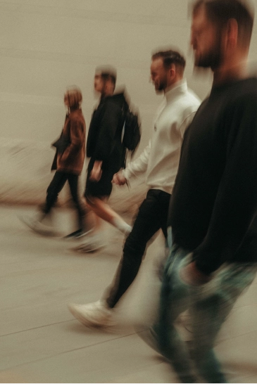 Four people walking past a plain wall in a blurred motion photograph.