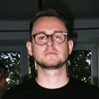 Portrait of a man with short brown hair and glasses wearing a black shirt indoors.