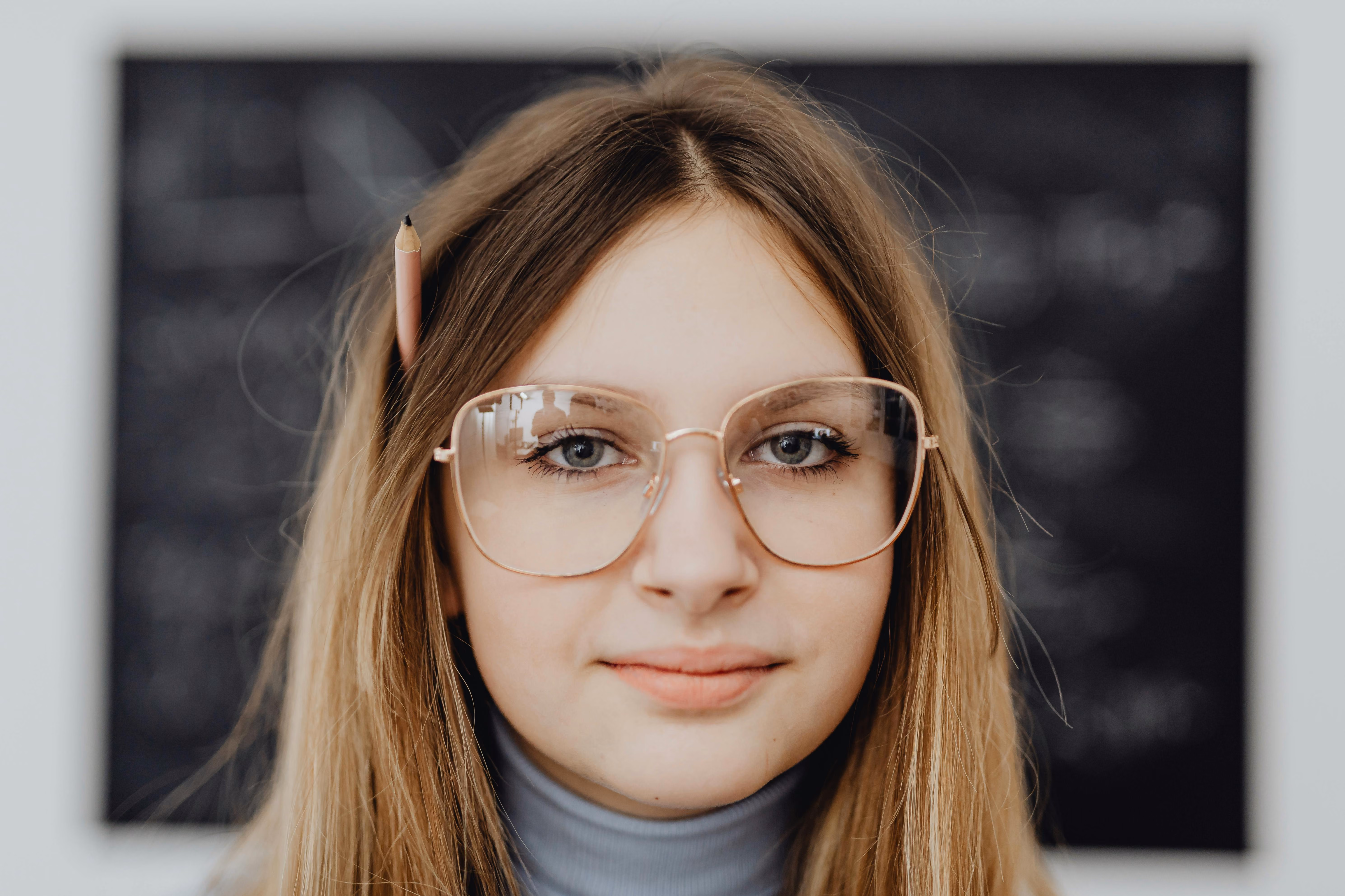 Student with glasses and pencil in hair stands before chalkboard