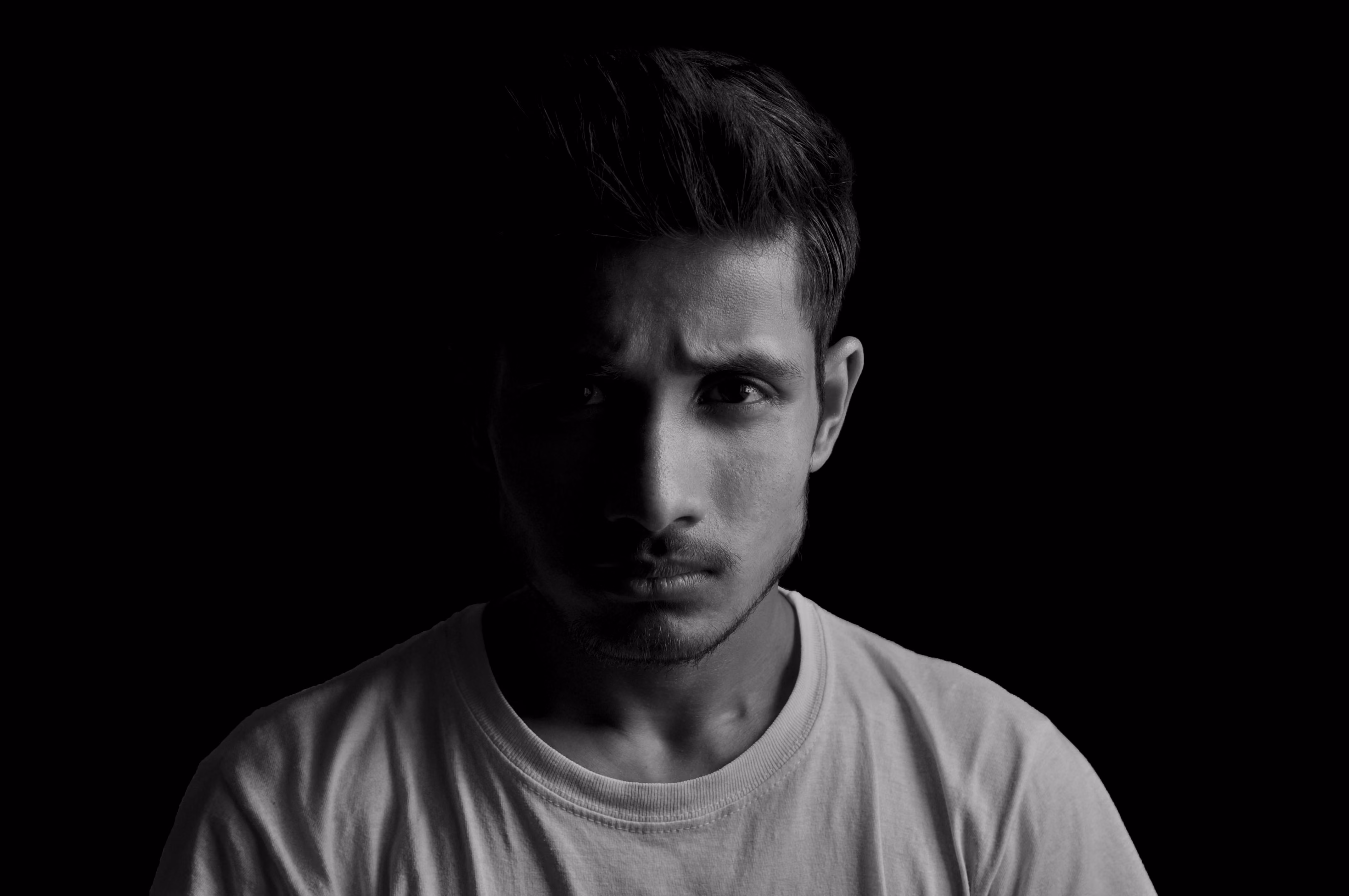 Black and white portrait of a young man with serious expression against a dark background.