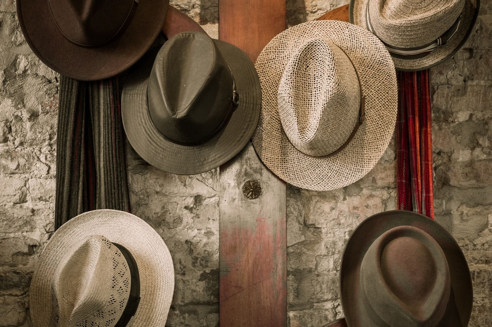 Various different hats hanging on a rustic wall representing T-shaped employees wearing multiple hats and multidisciplinary skills in growth companies