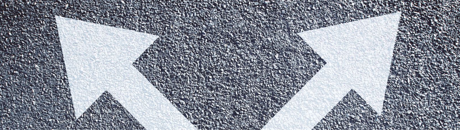 Two opposing white arrows painted on dark asphalt, representing the choice between RevOps and SalesOps for mid-market companies