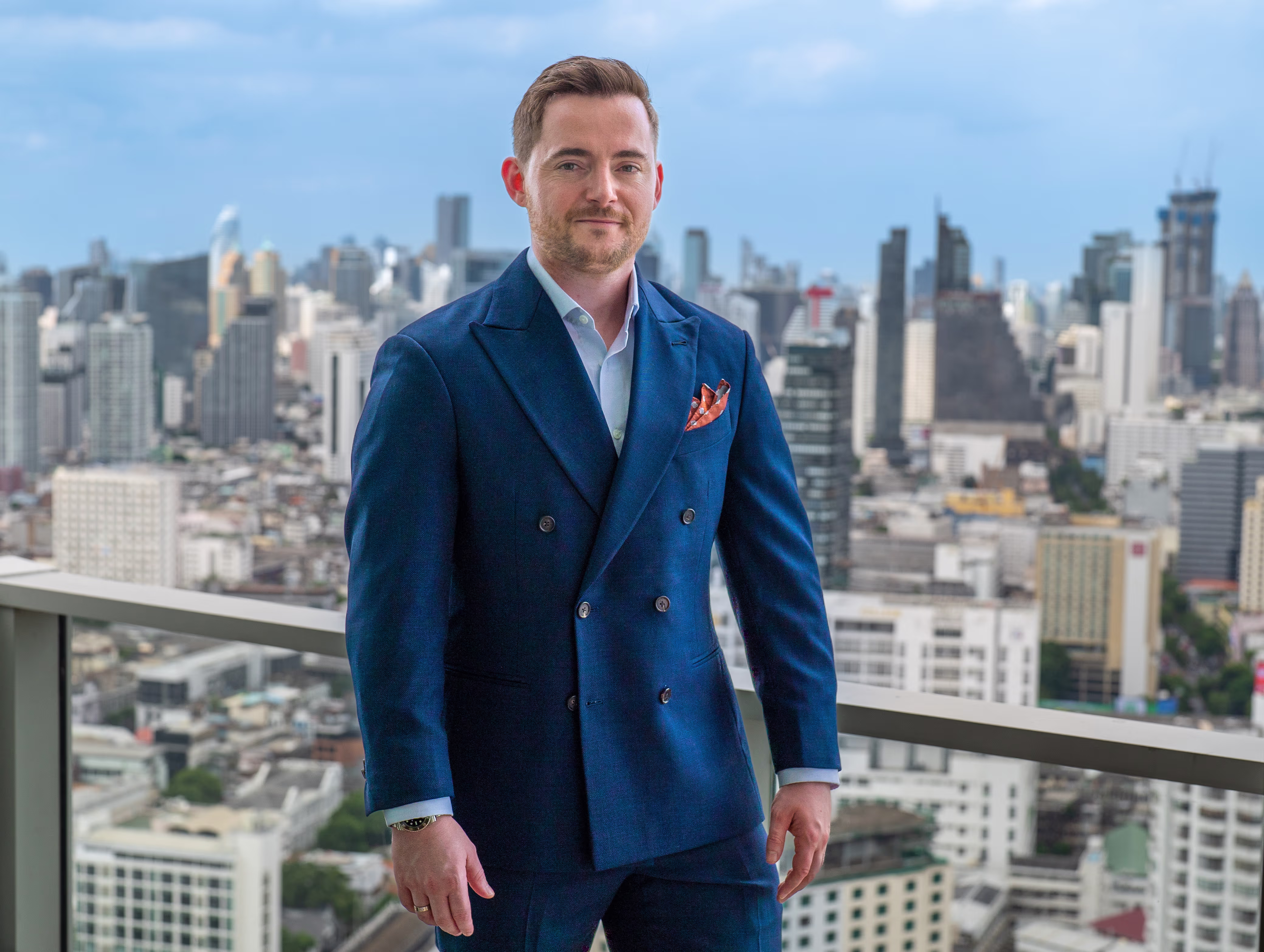 Leon Sylvester wearing a  dark blue suit jacket, city background.