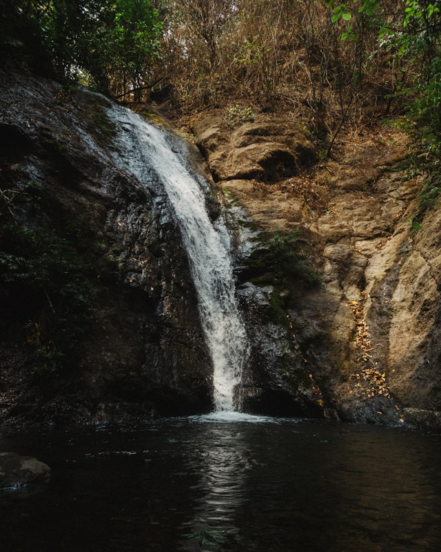 Waterval die langs rotsen naar beneden stroomt — symbool voor mijn eigen weg van kracht, kwetsbaarheid en voortdurende beweging.
