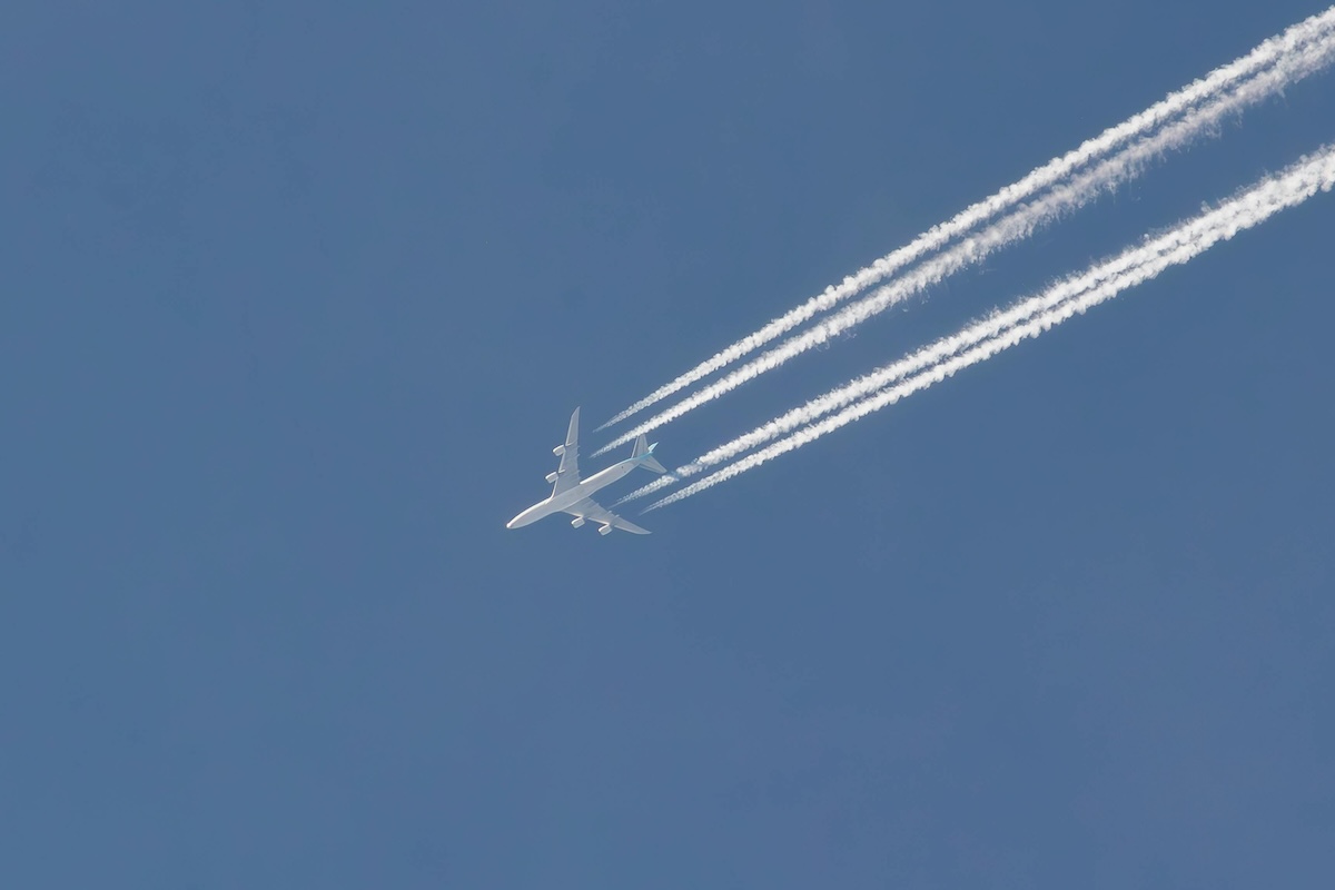 Airplane flying at high altitude with contrails against a blue sky.
