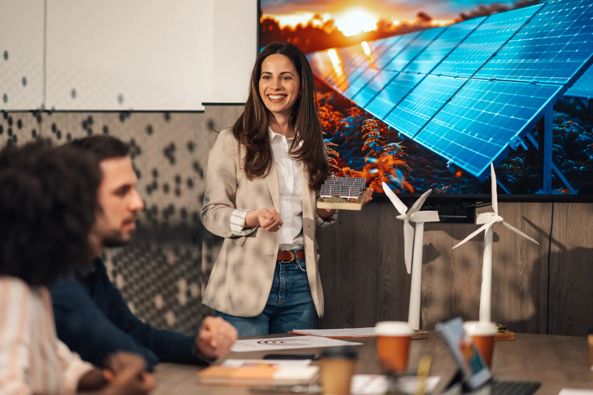 Woman presenting a solar model in front of a screen showing solar panels and wind turbines.
