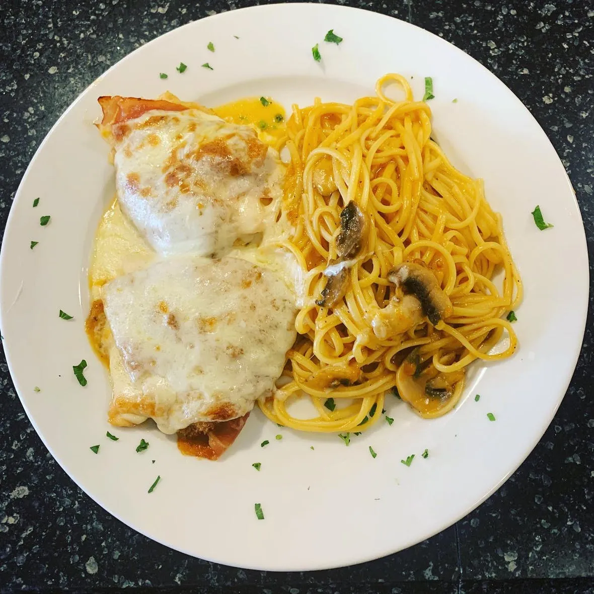 A white plate with a piece of chicken and spaghetti on it.