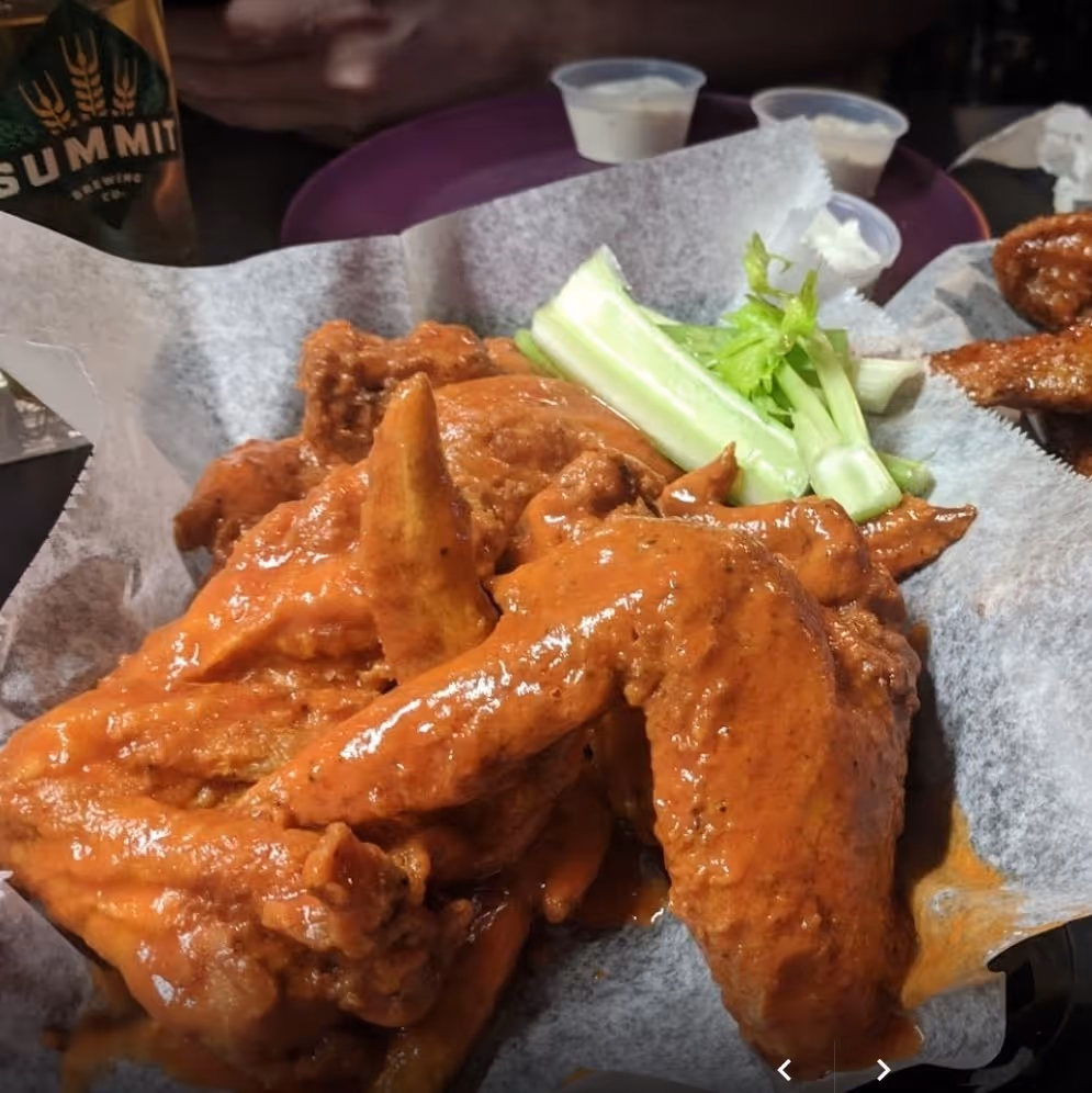 Crispy buffalo wings with celery sticks and savory sauce on a white plate.