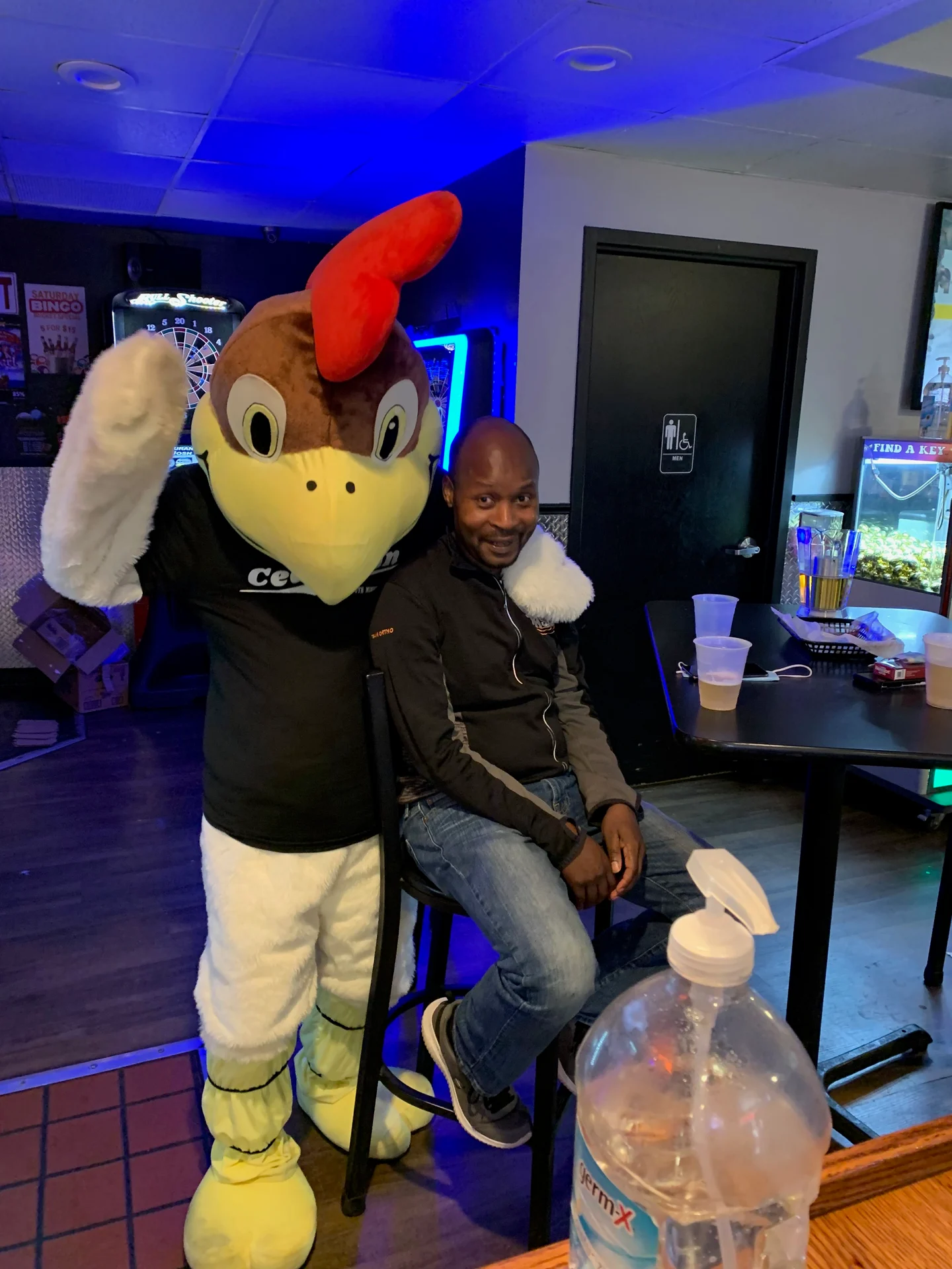 A man sitting next to a chicken mascot.