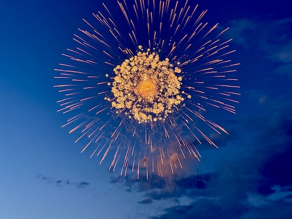 A large, bright orange firework explodes against a dark blue sky