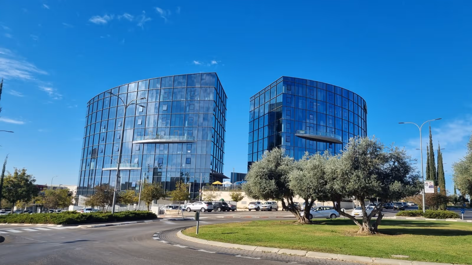 בנייני משרדים מודרניים עם חזיתות זכוכית ועצי זית בקדמה, סצנה אורבנית מישראל