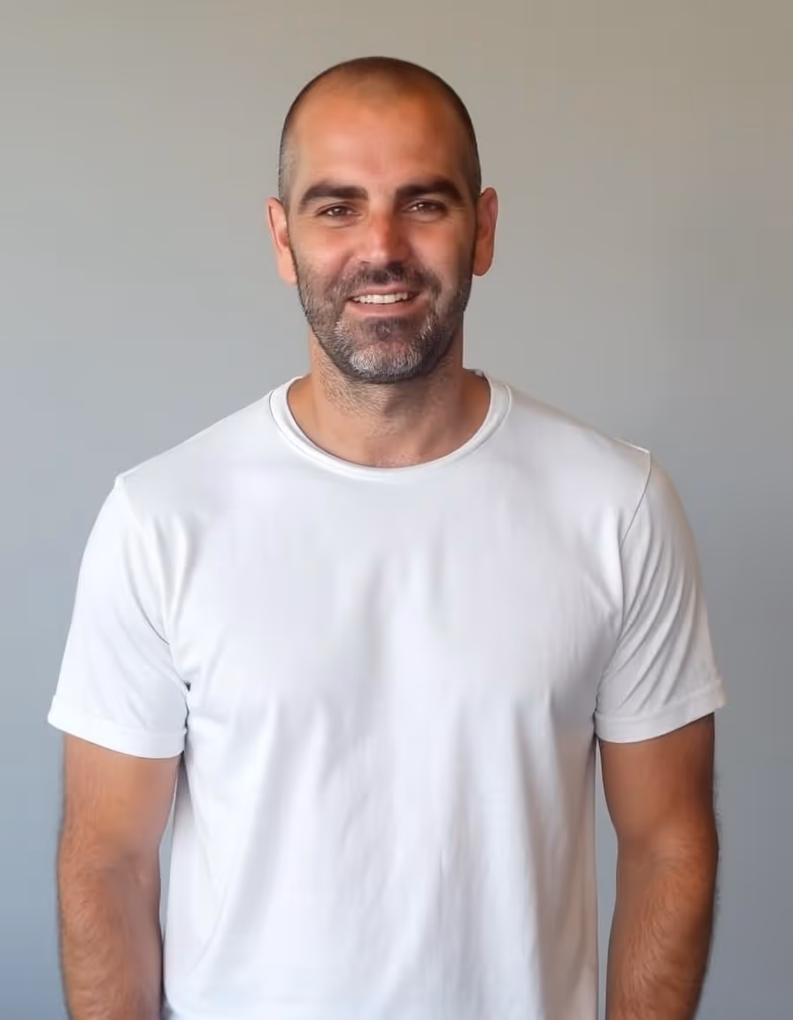 תמונה של עמית אהרוני, שמאי מקרקעין מוסמך, מחייך עם חולצה לבנה על רקע קיר אפור