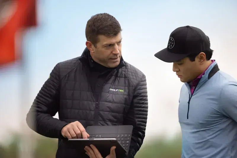 GOLFTEC coach showing player swing breakdown on laptop on the green