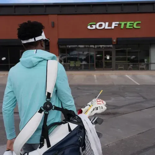 Student walking into GOLFTEC center with their clubs