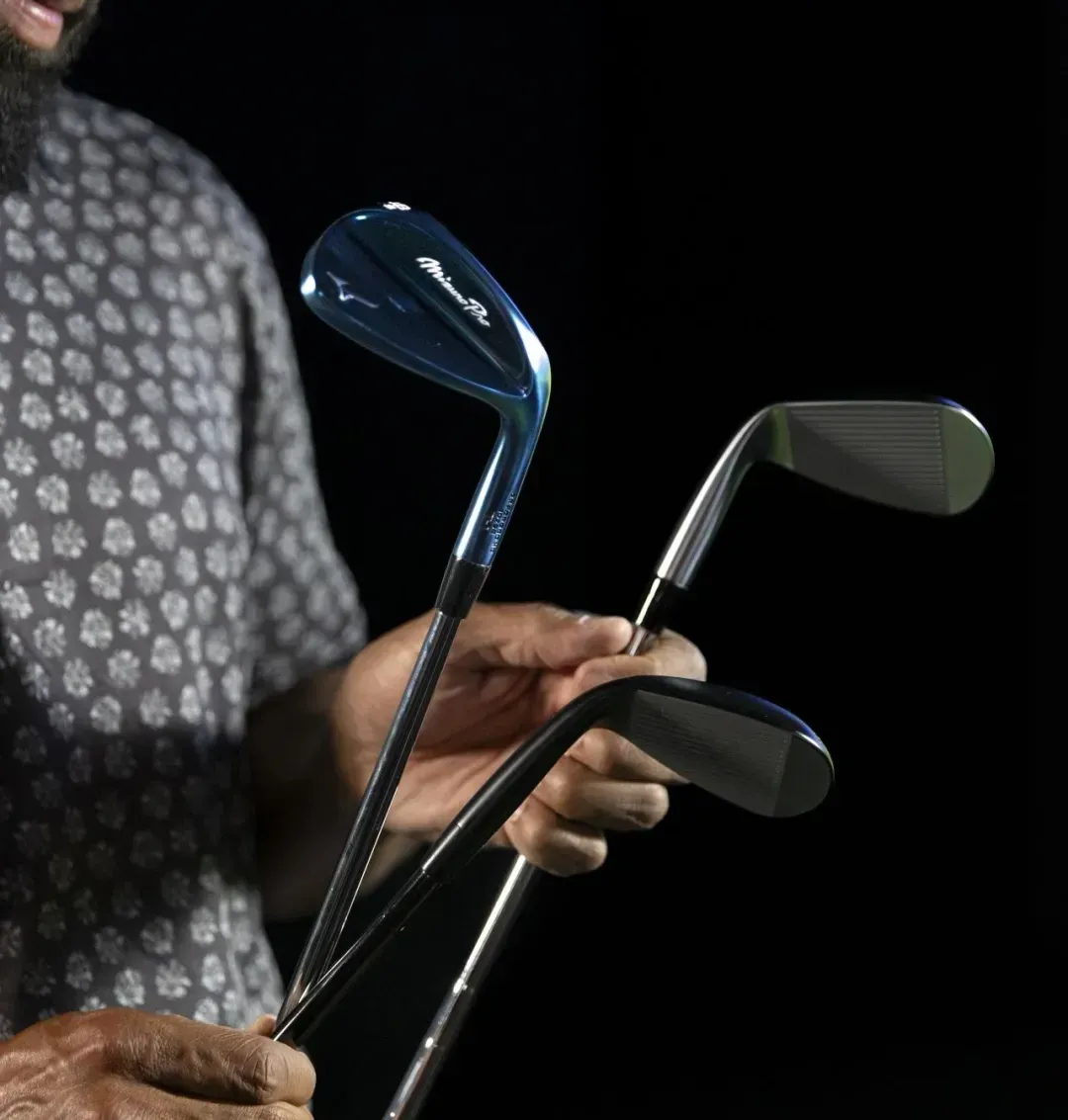 Golfer holding three different Mizuno Pro T-1 wedges, wearing a pattern shirt, with a black background to emphasize the clubfaces. 