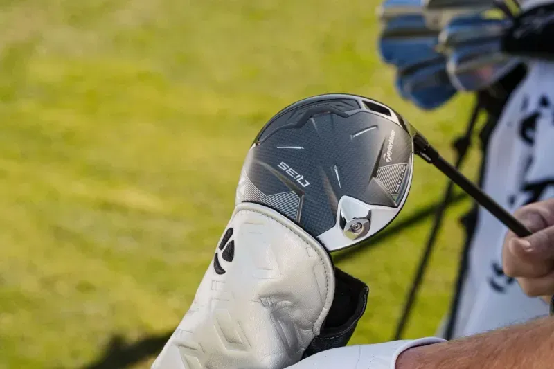 Golfer putting a TaylorMade Qi35 Driver into its head cover on the course, with the golf course setting in the background.