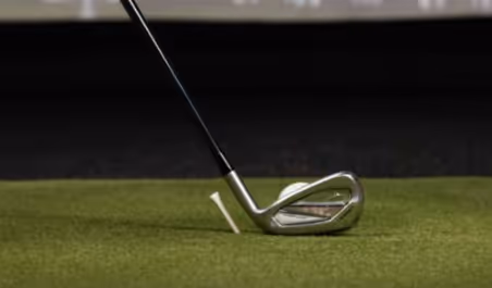 Iron aligned behind ball on turf beside tee for golf practice drill 